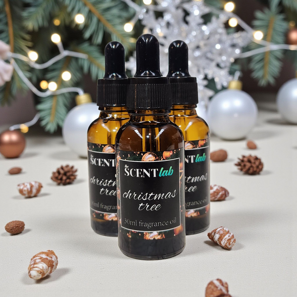 Three bottles of Scentlab Christmas tree fragrance oil with decorative elements on a light surface.