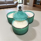 Three green textured glass candle holders with candles on a light surface.
